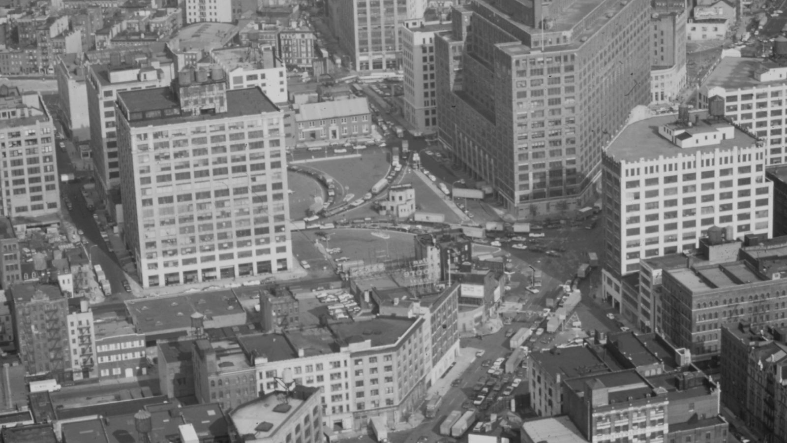 Archival aerial view of Lower Manhattan loft buildings around a traffic rotary crowded with trucks and cars