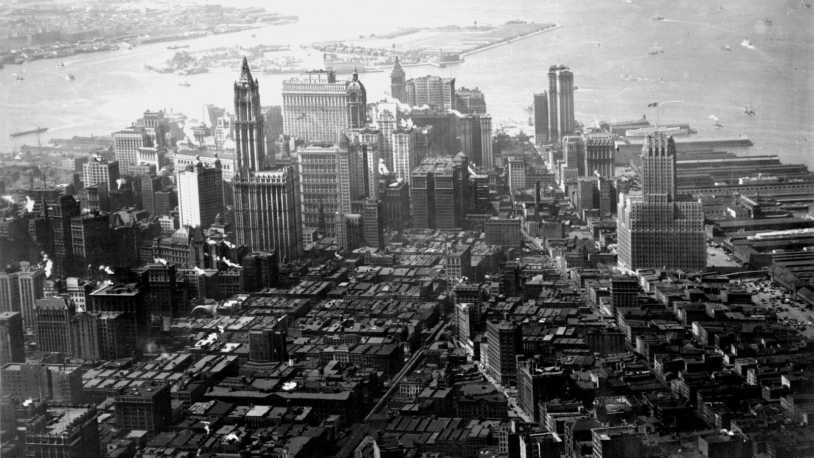 Archival aerial view of Lower Manhattan skyscrapers, including the Woolworth Building, with the harbor and Governors Island b