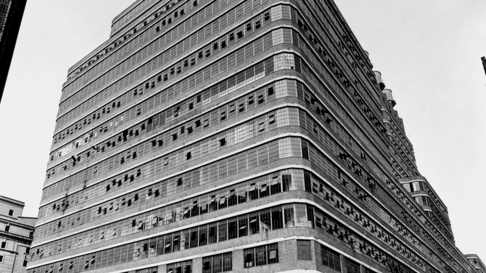 Black and white view looking up at a massive Manhattan industrial building with long horizontal bands of windows