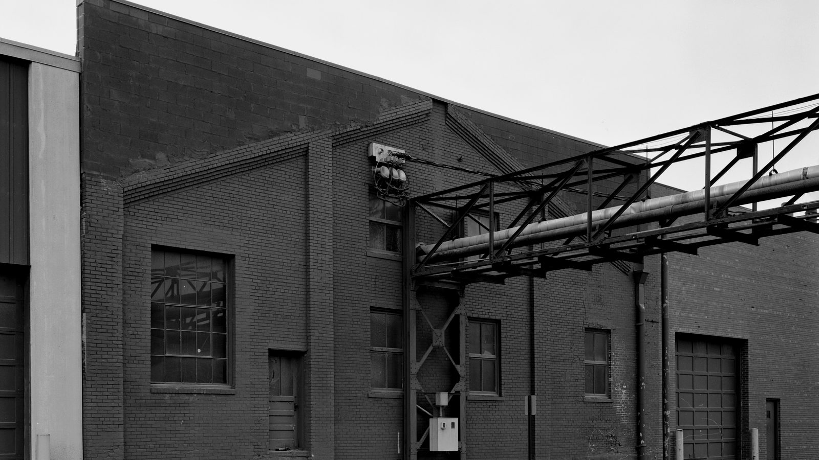 Brick industrial building with multi-pane windows, a loading door and a steel truss carrying pipes along its facade