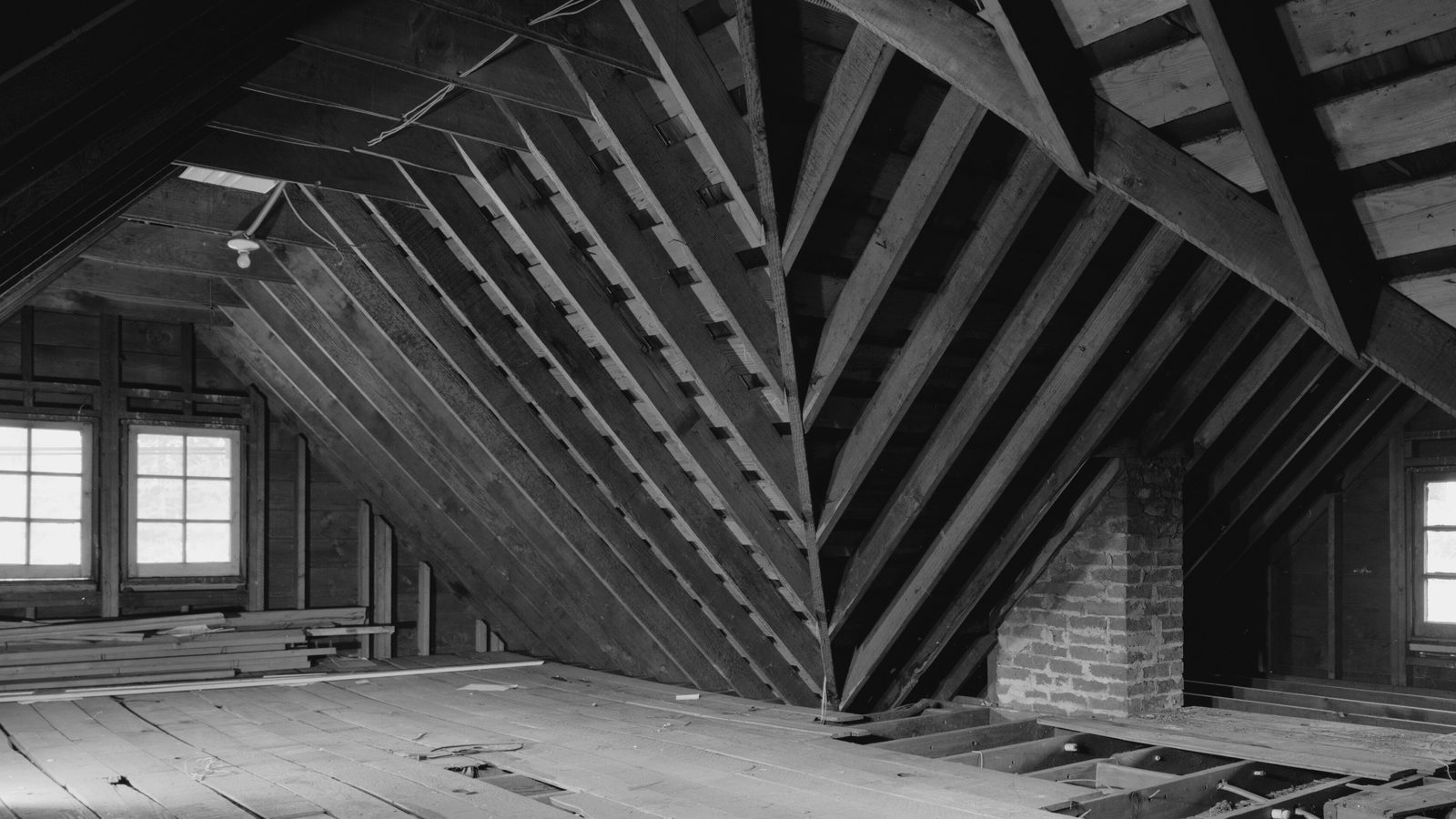 Unfinished wooden attic with exposed rafters, a brick chimney, small windows and open floor joists
