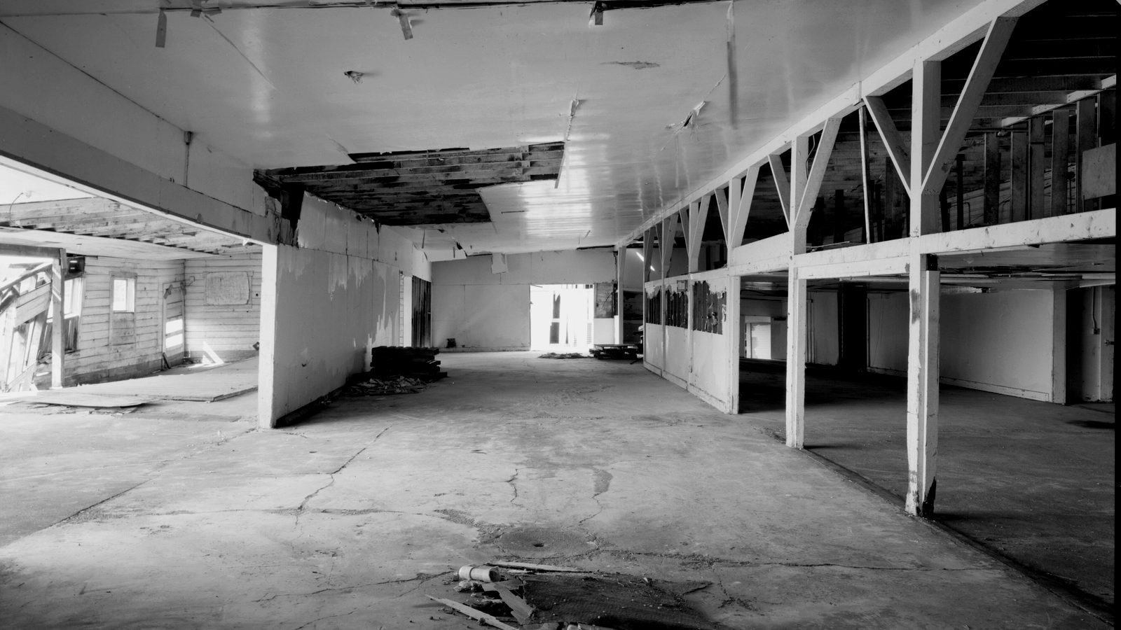 Empty commercial building interior with cracked concrete floor, damaged ceiling panels and exposed timber framing