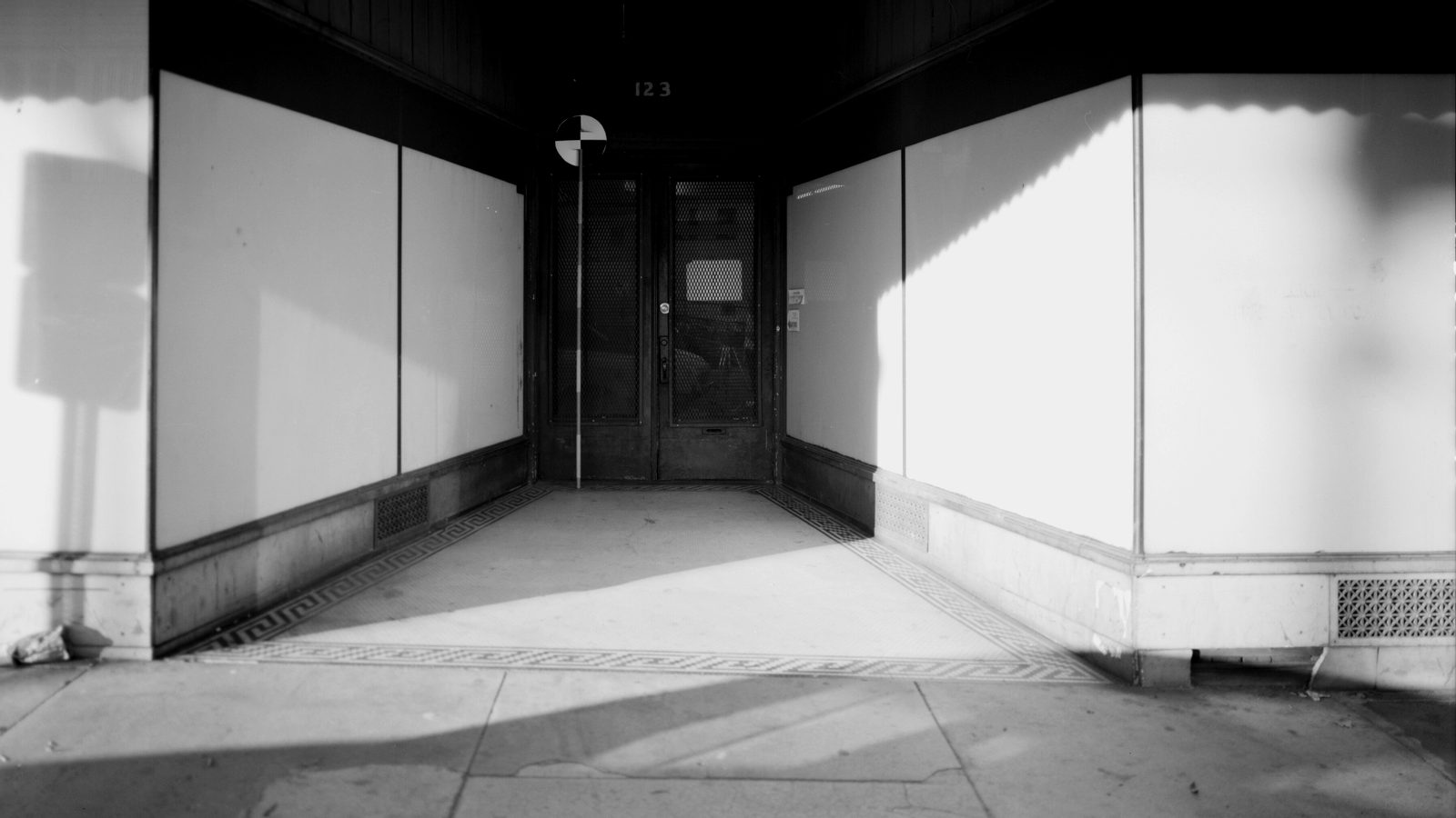 Recessed entrance of a vacant main street storefront with papered windows, double doors and a Greek key tile floor